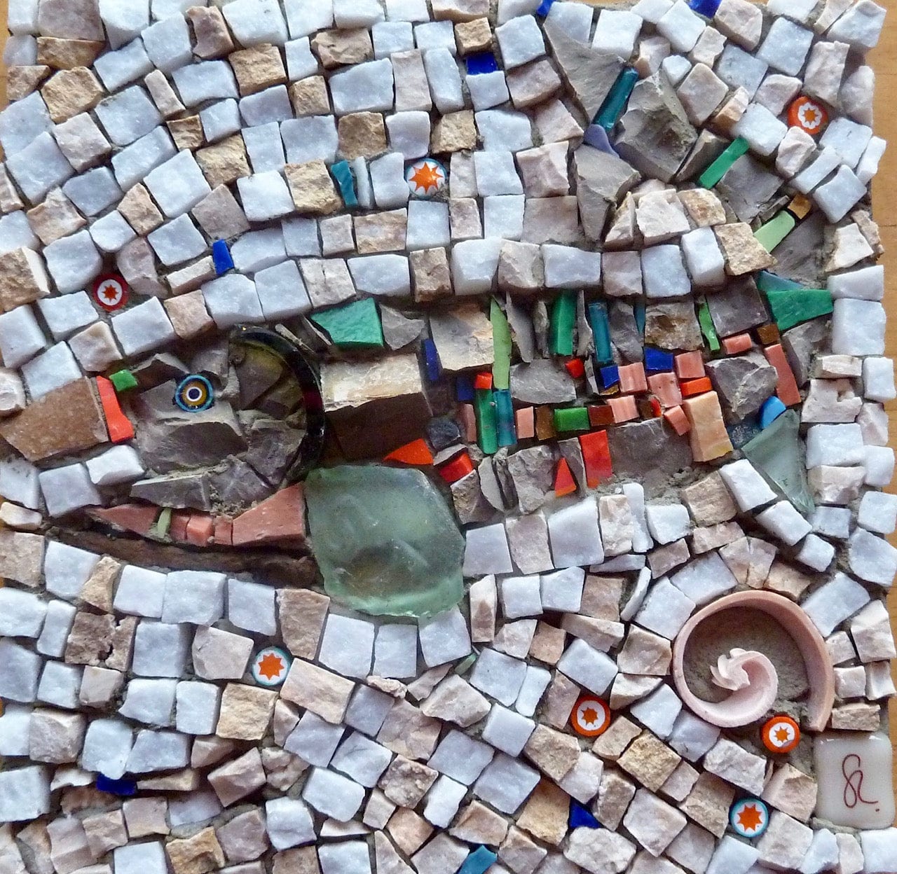 Mosaic artwork featuring pale stone tiles, colourful glass pieces and a spiral shell.